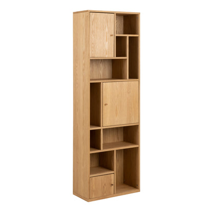 Narrow oak bookcase with asymmetrical open shelves and three closed storage compartments in a modern minimalist design.