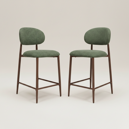 Two modern couter chairs with green upholstered seats and backs and dark brown wooden legs, shown on a light beige studio background.